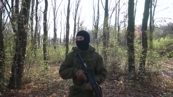 身着绿色制服 戴着黑色面具 头戴冲锋枪的士兵漫步在秋天的森林里 — 图库视频影像
