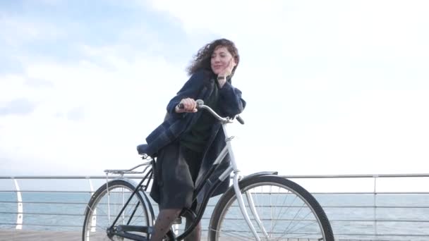 若いですStilishヒップスター女性ポージングで秋や冬のビーチでレトロな自転車 — ストック動画