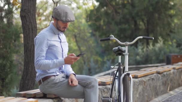 晴れた日に路上でレトロな自転車に乗って若いスタイリッシュな男性 携帯電話で現代のビジネスマンを肖像画 — ストック動画