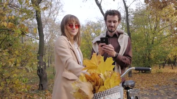 レトロな自転車で秋の公園を歩く若いスタイリッシュなカップル — ストック動画