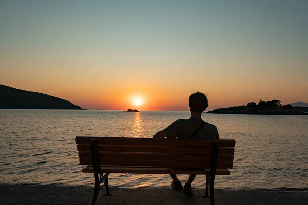 silhouette of male sitting on the bench and watching beautiful sunrise on the summer beach