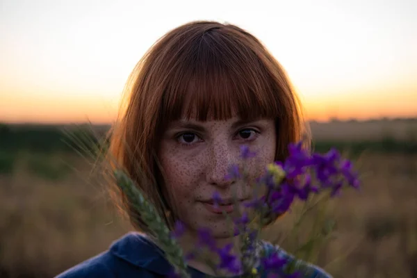 Young redhead woman with  freckles in vintage handmade dress walk in fields with flowers