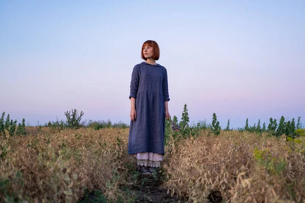 Young redhead woman with  freckles in vintage handmade dress walk in fields with flowers