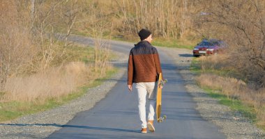 Genç bir erkek güneşli bir günde kaykayla kaykaya biniyor.