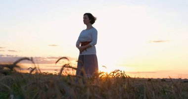 Kadın yaz tarlalarında qigong antrenmanı yapıyor ve arka planda güzel bir günbatımı var.