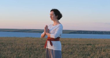 Kadın yaz tarlalarında qigong antrenmanı yapıyor ve arka planda güzel bir günbatımı var.