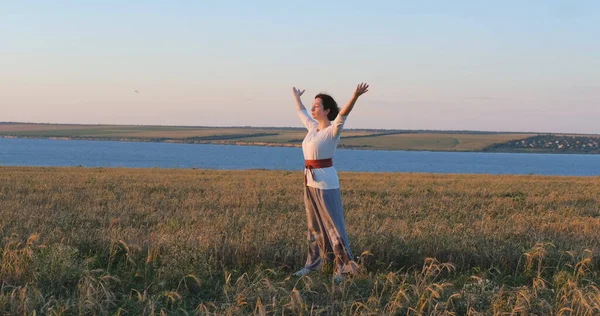 在有美丽落日背景的夏田里练习气功的女性 — 图库照片
