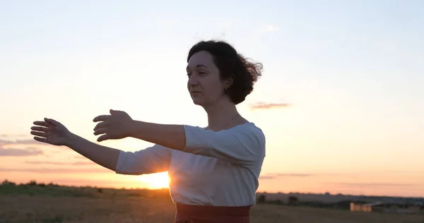 Kadın yaz tarlalarında qigong antrenmanı yapıyor ve arka planda güzel bir günbatımı var.