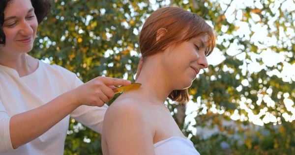 Woman do traditional chinese massage gua sha outdoors in summer garden