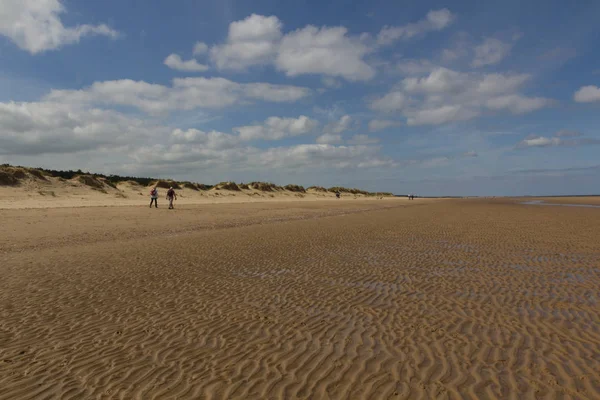 Песчаные дюны и люди, идущие по пляжу в Уэллс-рядом-с-морем — стоковое фото