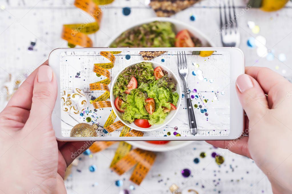 Woman taking photo of healthy salad on mobile phone. Trendy social networks photo shoot. Copy space. Top view, flat lay style