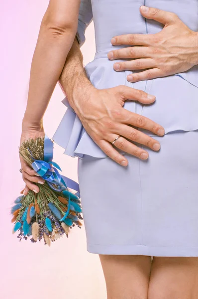 hands of a man hugging the waist of a girl with a bouquet