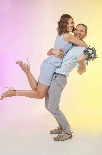 joyful couple in pastel-colored clothes, the husband is holding his wife in his arms with a bouquet