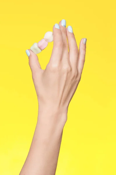 Female hand with fashion manicure. Gelatin candies on a stick on a yellow background