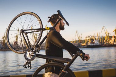 Günbatımı ve gündoğumu liman arka plan üzerinde ile sırasında omzunda Bisiklet ile yürüyen şık yakışıklı adam