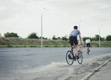 Genç hipster adam yolda toz içinde sabit vites bisiklet sürme