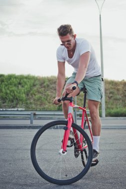 Genç yakışıklı hipster kişini Sabit vites bisiklet günbatımı sırasında