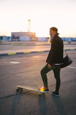 Günbatımı kentsel arka plan üzerinde sırasında longboard ile uzun gri sakal ayakta olan şık yakışıklı orta yaşlı adam