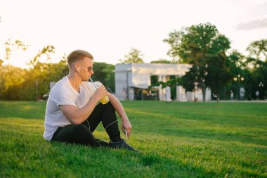 Yakışıklı genç hipster adam açık havada park limonata içmeye kulaklık ile 