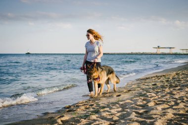 Alman çoban köpeği ile açık kumsalda yürüyen mutlu genç kadın