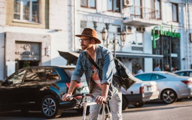 Genç şık hipster adam şapka ve gözlük güneşli günde Bisiklete binmek şehir merkezinde