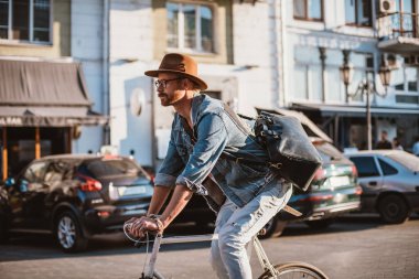 Genç şık hipster adam şapka ve gözlük güneşli günde Bisiklete binmek şehir merkezinde