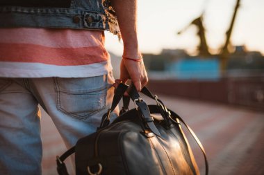 Çantayla günbatımı sırasında deniz bağlantı noktası arka plan üzerinde yürüyen genç şık hipster yakın çekim