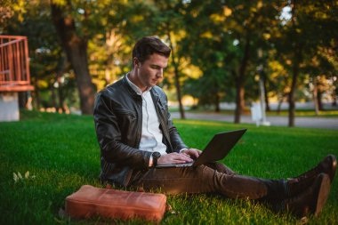 Yakışıklı delikanlı Park çimenlerin üzerinde döşeme dizüstü bilgisayar kullanarak