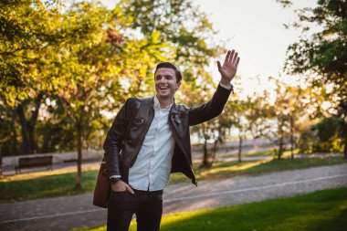 Yakışıklı delikanlı güneşli gün boyunca, Sonbahar Tema parkında el sallayarak bir çanta