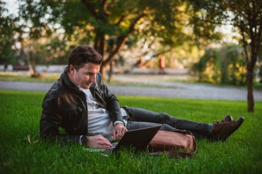 Yakışıklı delikanlı Park çimenlerin üzerinde döşeme dizüstü bilgisayar kullanarak