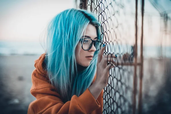 Mavi saçlı ve gözlüklü mesh çit yakınındaki plajda oturmuş olan genç hipster kadın portresi