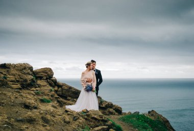 Arka plan açık havada okyanusun bir uçurumun üzerinde duran genç düğün çifti