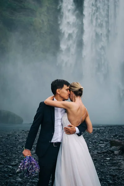 Young wedding couple hugging under rain on background of waterfall