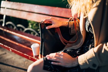 Kahve ve deri çanta ile parkta bankta oturan kadının yakın çekim