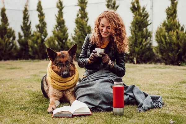 Mutlu genç kadın termos fincan tutan ve çim onu Alman çoban köpeği ile oturan, açık