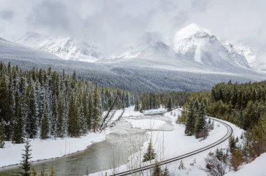Donmuş bir Nehri'nin bir karlı dağ manzarası demiryolundan bulutlu bir kış gününde eğme. Banff Ulusal Parkı, Ab, Kanada.