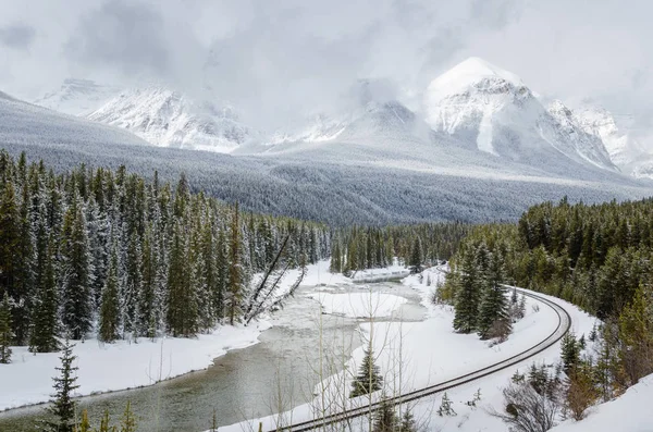 在多云的冬日里 一条结冰的河流上的冰冷的河岸边的铁轨弯曲 加拿大 班夫国家公园 — 图库照片