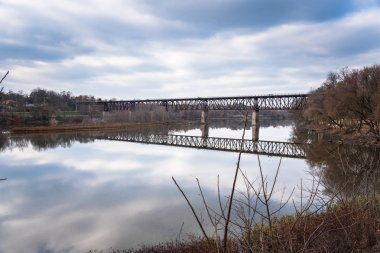 Paslı çelik demiryolu köprüsü üzerinden bir sonbahar gününde bir nehir. Sakin sularda büyük yansıma