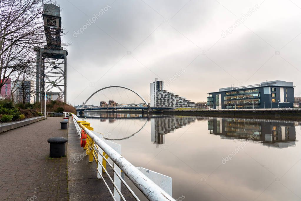 River Clyde in Glasgow fromt the Riverbank Footpath on a Cloudy Winter Day. A Modern Road Bridge is Visible in Distance. Reflection in Water.