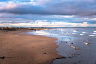 Güzel bir kış gün batımı keyfini bir güzel Sandy üzerinde yürüyen insanlar. St Andrews, Scotland, İngiltere.