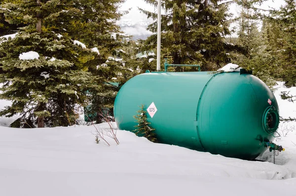 Big Green Propane Tank in a Backyard Covered in Snow with Pine Trees in Background