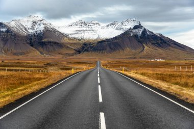 İzlanda bir bulutlu sonbahar gününde çok yüksek karla kaplı dağlara boş yol