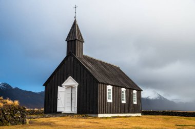 Siyah ahşap kilise İzlanda bir bulutlu sonbahar gününde arka planda güzel karla kaplı dağlar