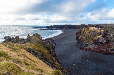 İzlanda'daki bir uçurumun tepesine bir siyah plaj görünümünü bir bulutlu sonbahar gününde. Visible Beach yürüme okyanusa doğru üzerinde iki kişi vardır