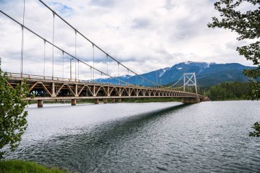 Eski otoyol asma köprü Dağı bulutlu bir yaz gününde arka planda bir geniş nehir üzerinde. Revelstoke, Bc, Kanada.