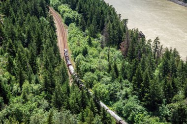 Güneşli bir yaz gününde bir nehir yanında throgh Woods çalışan bir demiryolu hattı üzerinde bir yük treni havadan görünümü. Fraser River Gorge, BC, Kanada.