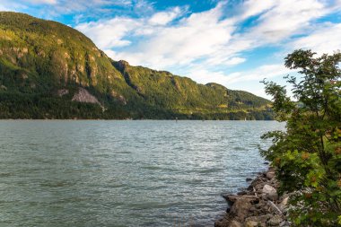Arka planda yükselen ormanlık dağlar ile bir Bay görünümü sıcak bir ayar güneş tarafından yaktı. Squamish, BC, Kanada.