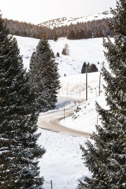Bulutlu bir kış gününde Avrupa Alpleri'nde karla kaplı boş dolambaçlı AlpLer Yolu. Tehlikeli sürüş durumu kavramı.