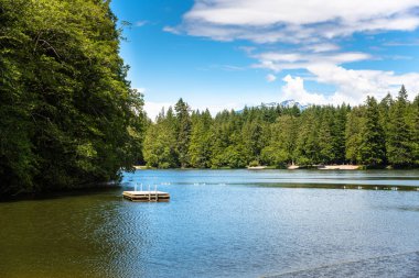 Ön planda ve din adamları gökyüzünde boş bir ahşap yüzme platformu ile güzel dağ gölü görünümü. Squamish, Bc, Kanada.