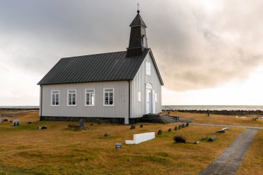 Gün batımında bulutlu gökyüzü altında İzlanda kıyıları boyunca Lonely Chapel